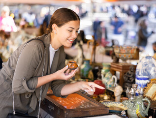 Smiling female tourist checking out small clay cup at flea market