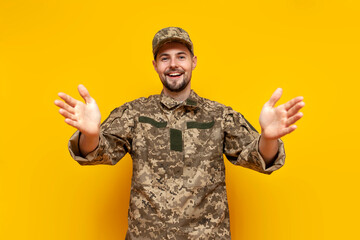 young ukrainian male soldier in camouflage uniform pixel shows hug and welcome on yellow isolated...