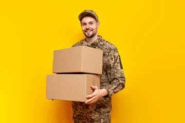 young Ukrainian male soldier in camouflage pixel uniform holding a box on a yellow isolated...