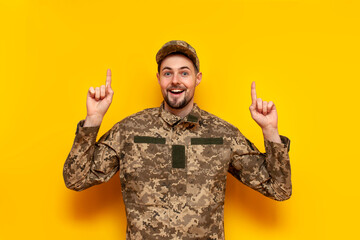 young Ukrainian male soldier in camouflage pixel uniform points his hands up on a yellow isolated...