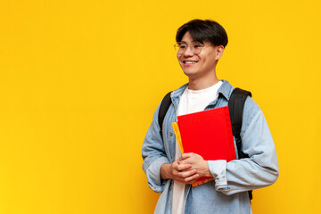 asian young male student in glasses with backpack holding books and going to study on yellow...