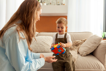 young mother gives toy car to her little son, 2-year-old boy holds children's toy, woman plays with child