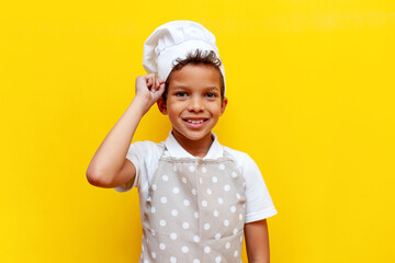 african american boy in uniform and chef's hat smiling on yellow isolated background, teenager...