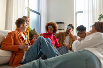 multiracial group of young people sitting at home with beer and popcorn and playing charades and having fun with friends, students of different ethnicities at home playing games and celebrating - obrazy, fototapety, plakaty