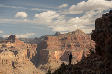 Silhouetted Hiker Stands With Hand Raised While Looking Out Over Grand Canyon