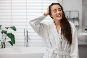 Smiling woman wearing bathrobe after shower in bathroom. Space for text