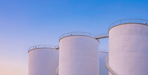 Group of white storage fuel tanks in petrochemical industrial area against dusk sky background in evening time