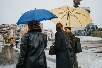 Business partners discussing project on a rainy day in the city, using an umbrella to stay dry while working together towards business expansion and profit growth.