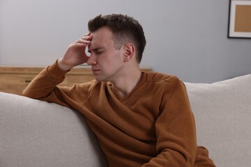 Sad man suffering from headache on sofa indoors