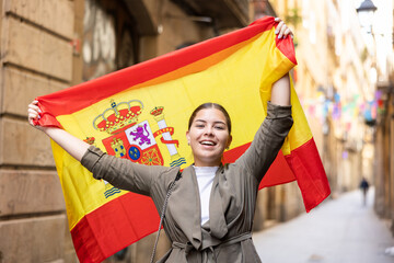 Patriotic young woman waving the flag of Spain on the city street - obrazy, fototapety, plakaty