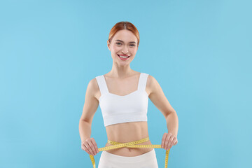 Slim woman measuring waist with tape on light blue background. Weight loss
