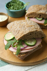 Tasty sandwiches with boiled sausage, cucumber, arugula and sauce on table, closeup