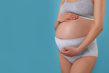 Fototapeta na wymiar Pregnant woman in comfortable maternity underwear on light blue background, closeup. Space for text