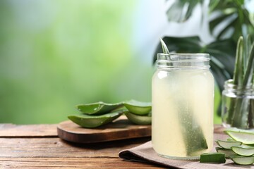 Fresh aloe juice in jar and cut leaves on wooden table outdoors. Space for text