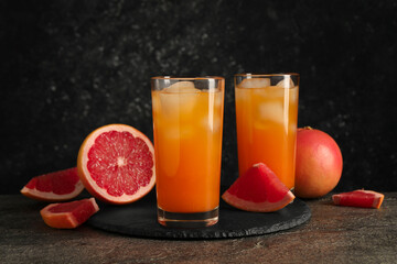 Tasty grapefruit drink with ice in glasses and fresh fruits on dark textured table