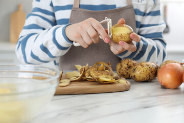 Woman peeling fresh potato at white marble table indoors, closeup