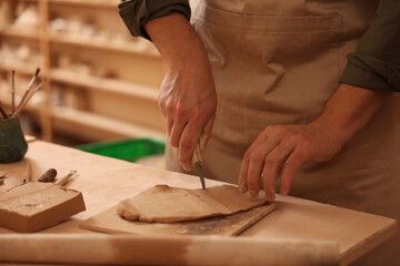 Man cutting clay with knife at table indoors, closeup