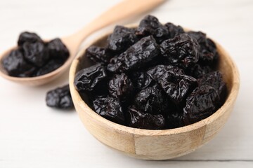 Bowl and spoon with sweet dried prunes on white table, closeup