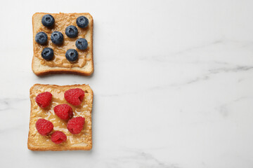 Delicious toasts with peanut butter, raspberries and blueberries on white marble table, flat lay. Space for text
