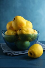 Tasty ripe quinces in bowl on blue wooden table