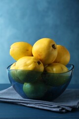 Tasty ripe quinces in bowl on blue wooden table