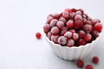 Frozen red cranberries in bowl on light table, closeup. Space for text