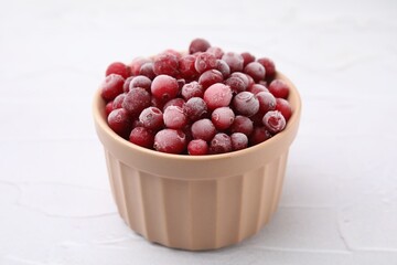 Frozen red cranberries in bowl on white table, closeup