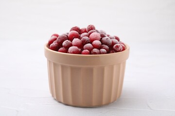 Frozen red cranberries in bowl on white table, closeup