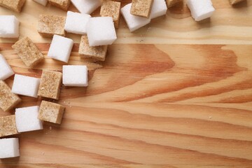 White and brown sugar cubes on wooden table, flat lay. Space for text