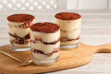 Delicious tiramisu in glasses and spoon on light wooden table, closeup