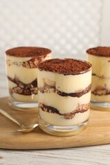 Delicious tiramisu in glasses and spoon on light wooden table