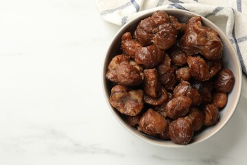 Roasted edible sweet chestnuts in bowl on white marble table, top view. Space for text