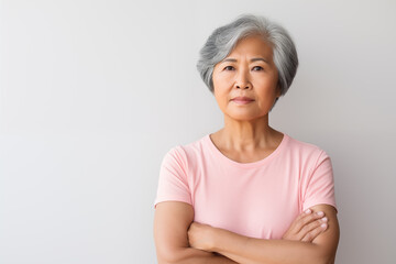 senior Asian American woman concerned expression wearing a light pink t shirt  in soft light with plain gray background