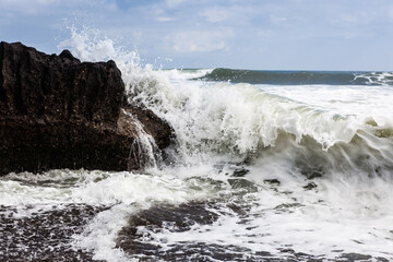 Wave crashing against a rock on a black coast, showcasing the ocean's power.