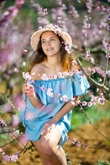 Lovely girl in hat and blue dress in spring peach garden