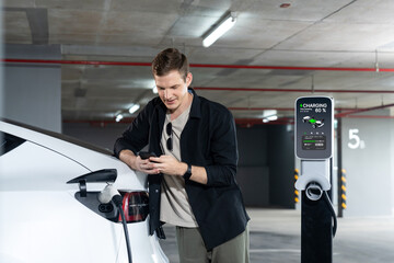 Young man travel with EV electric car to shopping center parking lot charging in downtown city...