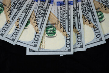 Partial view of 100 US dollar notes on a dark background.	