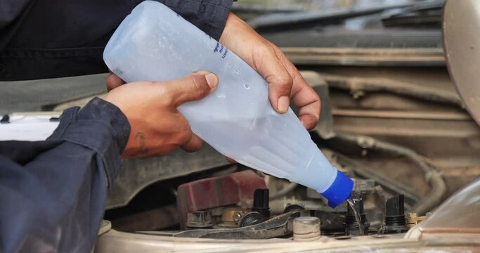 Car Mechanic man hands pouring Deionized purified Distilled water for car battery mechanical service. Close up hands man hold Deionized Distilled liquid water bottle at garage auto mobile car service