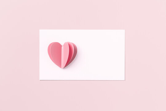 Pink cute cut heart and clean white paper for love note on pink colored background. Minimal trend flat lay, pastel color, mock up valentine Day card or wedding invitation. Romantic concept