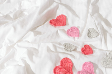 Pink red knitted valentine hearts on bed on white crumpled sheet. Minimal style flat lay photo, Valentine's Day, romantic relationship, love, wedding concept, top view card, tender pastel