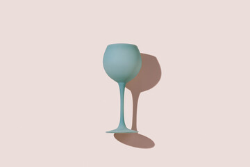 Pastel blue gray colored wine glass and sun shadow on colors background. Minimal style flat lay event or party concept. Aesthetic top view stylish wineglass, trend photo of summer cocktail drink