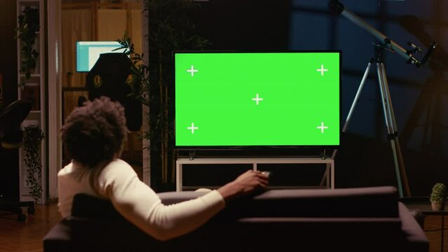 Person using chroma key video projector to binge series on subscription based streaming services. Cord cutter relaxing on couch, enjoying video on demand shows on mockup smart TV