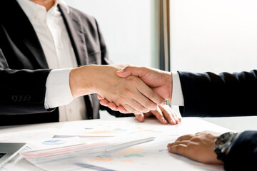 Entrepreneurs collaboration deal shaking hands in a modern office and financial paper graph on desk. - obrazy, fototapety, plakaty