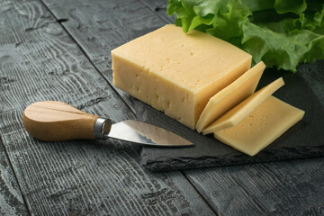 Lettuce leaves, a large piece of cheese and a knife on a wooden table.