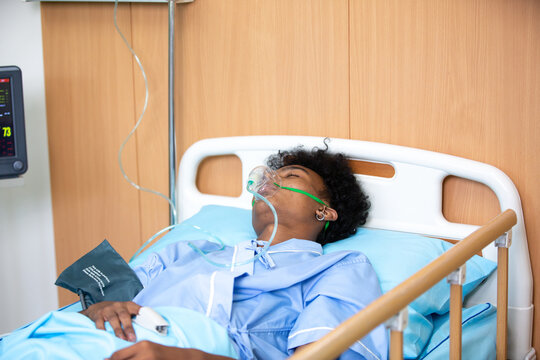 Closeup of an African American young adult patient getting medical treatment or using respirator for breathing, aid for an emergency, cancer Sick, ICU, injury, virus or ill boy lying on a hospital bed