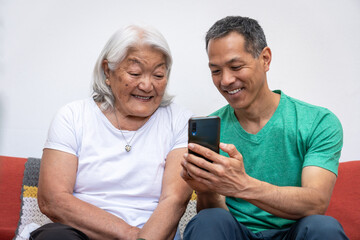 Adult son teaching his elderly mother of Japanese origin how to use a mobile phone.