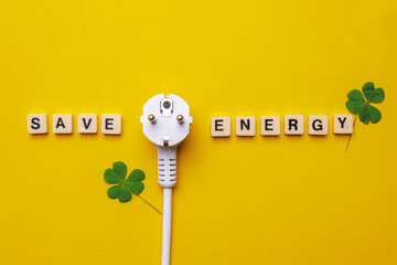 Save Energy words written on wooden cubes with electric plug and leaves over yellow background.  Saving energy and eco friendly concept