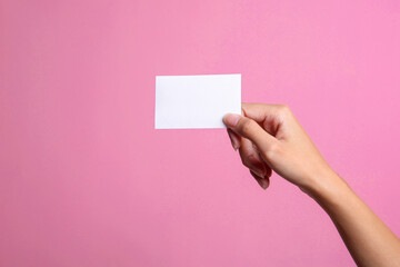 Female hand holding white blank business card mockup isolated pink background