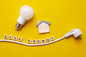 Save Energy written on wooden blocks, electric plug, light bulb and a house symbol on yellow background. Concept saving energy at home