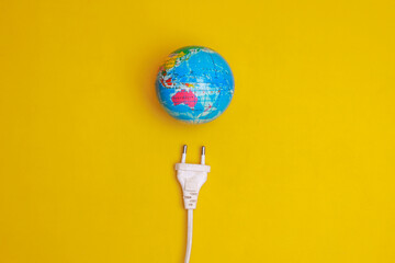 Globe with an electric plug on yellow background. Concept of power saving save the planet